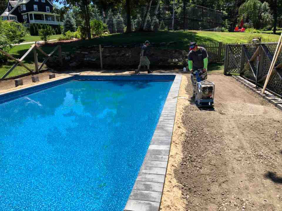 Construction crew preparing patio sub-base with proper grading and compaction equipment - Custom Patio Builder
